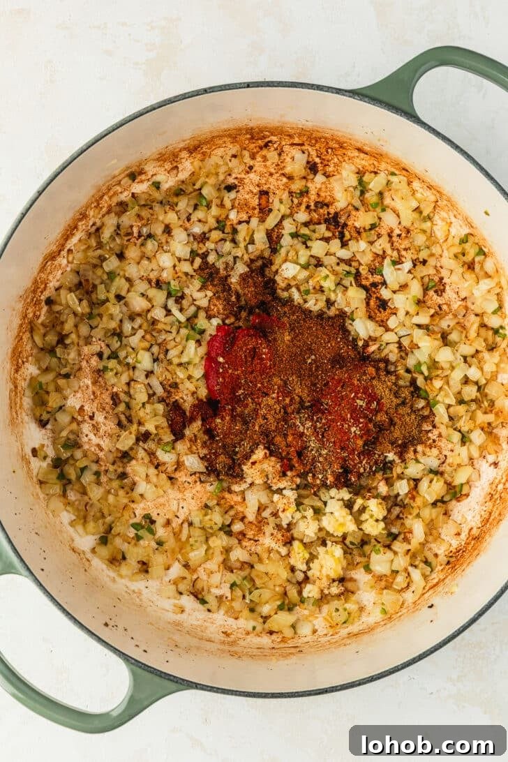 A green Dutch oven of onions, jalapenos, and spices on a tan counter.