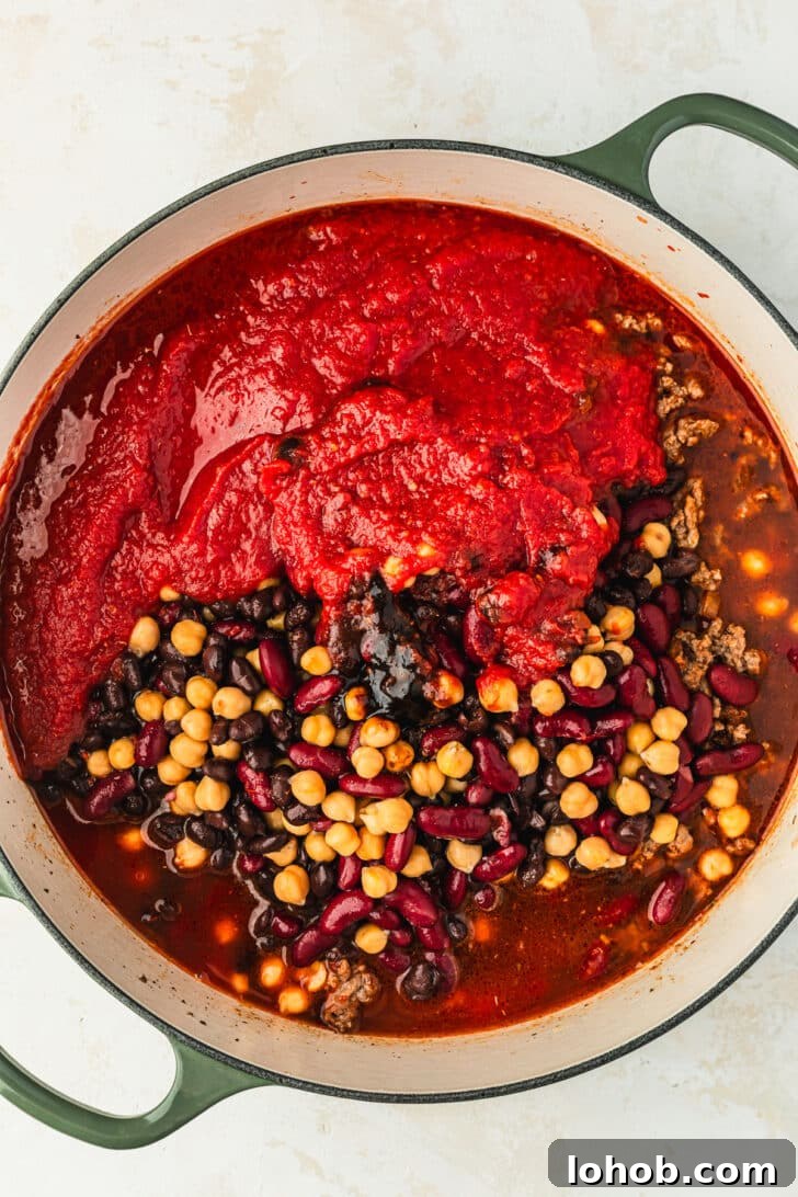 Ingredients for three bean chili in a green Dutch oven on a white counter.