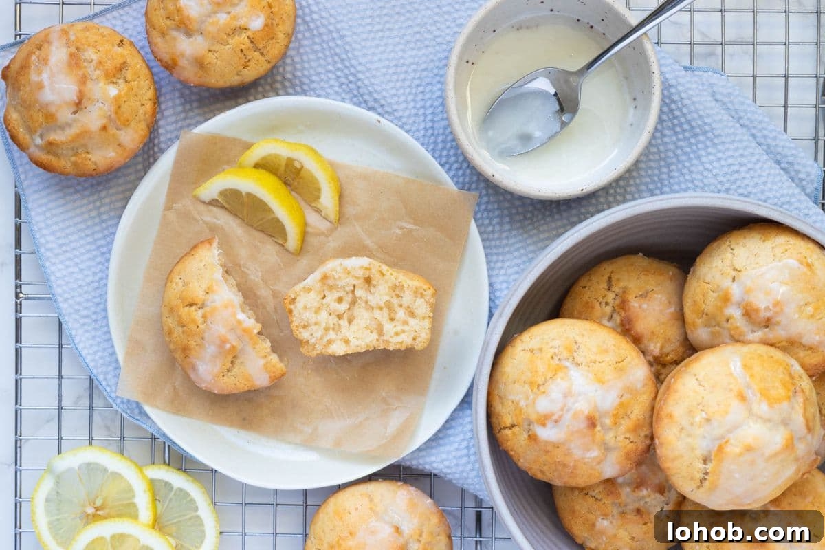 Quick Sourdough Lemon Muffins Recipe for Fresh Morning Bakes 2 Sourdough lemon muffins with lemon glaze served with lemon slices on a plate.