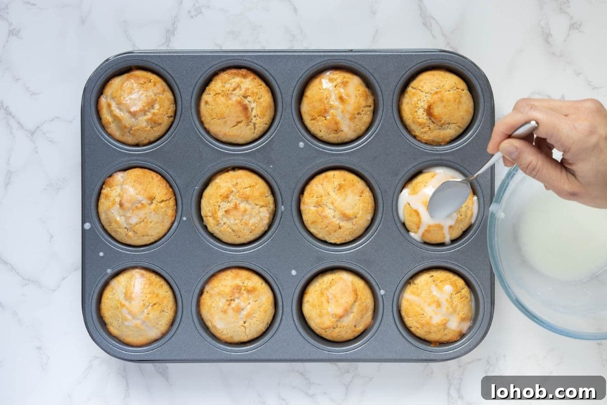 Quick Sourdough Lemon Muffins Recipe for Fresh Morning Bakes 9 Lemon glaze being spooned over freshly baked sourdough lemon muffins in a muffin pan.