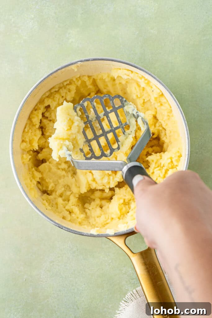 Classic Cottage Pie Recipe with Savory Beef and Mashed Potato Top 10 Mashing the potatoes in a pot.
