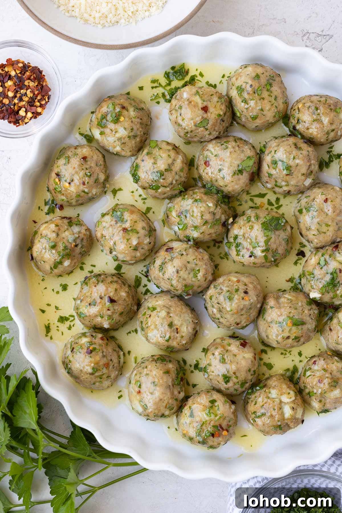 Oven-Baked Turkey Meatballs with Tangy Tomato Sauce 2 Turkey meatballs in a butter, olive oil, garlic sauce in a white dish with parsley.