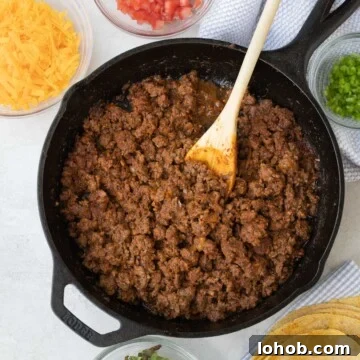 Taco meat in a cast iron pan with fixings for tacos around it.
