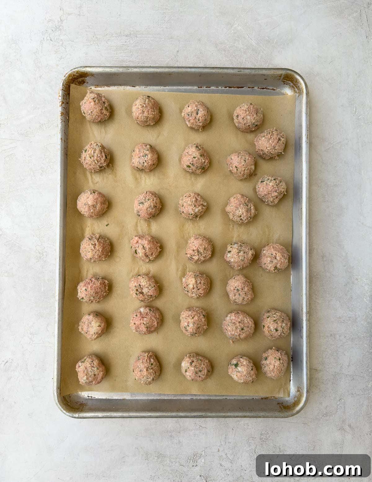Oven-Baked Turkey Meatballs with Tangy Tomato Sauce 8 Rolled meatballs on a rimmed baking sheet with parchment for oven baking.