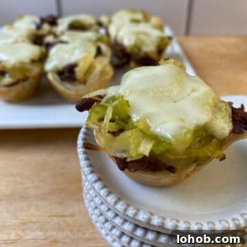 15 Cozy Appetizers for Cold-Weather Entertaining 2 Philly Cheesesteak bite on a small stack of dishes with the serving plate in the background.