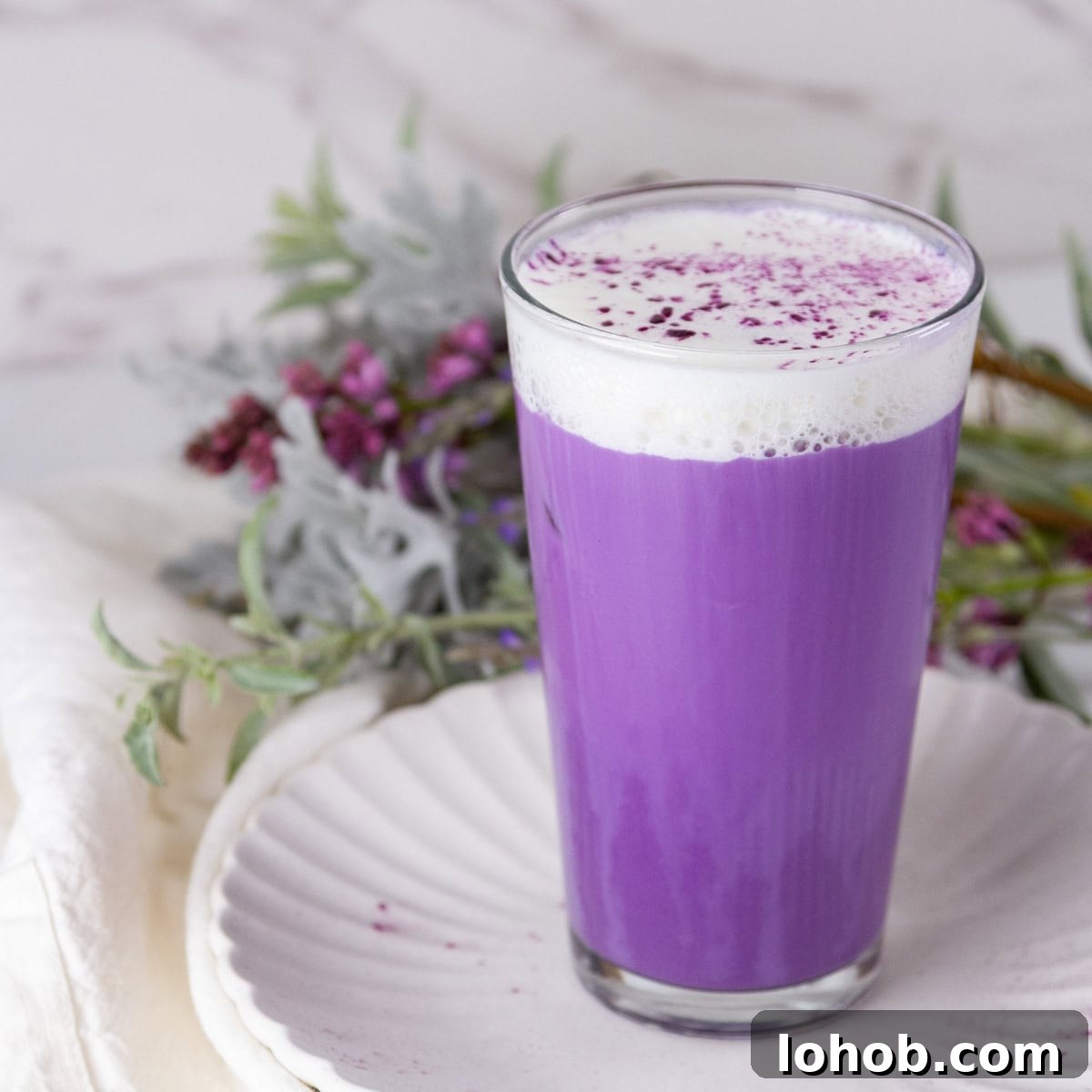 Alcohol-Free Drinks: Creative Mocktails & Refreshing Alternatives 9 square crop of an iced ube latte with cold foam in front of some flowers.