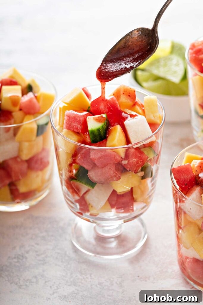 A spoon drizzling chamoy sauce over fresh fruit pieces in a glass cup
