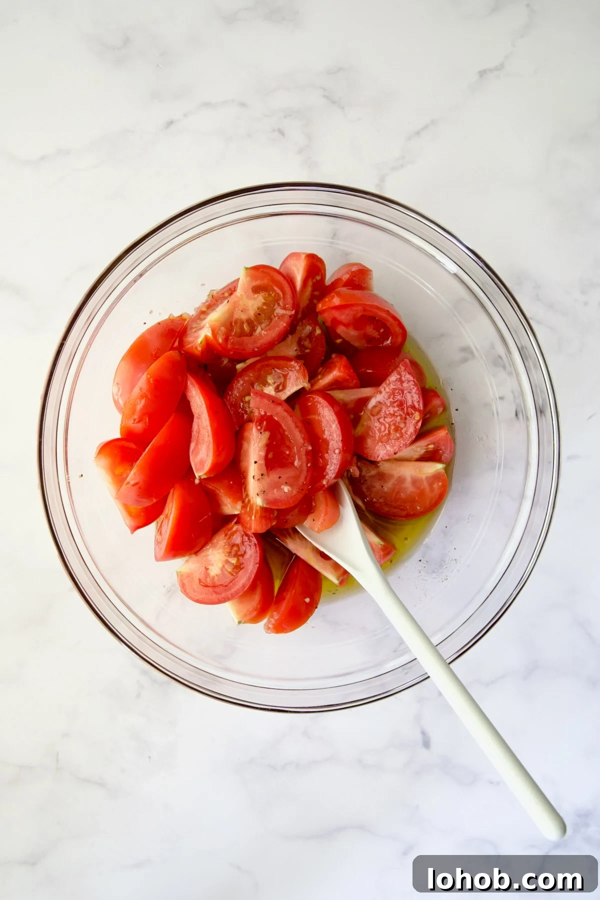 Quick-Pickled Marinated Tomatoes for Fresh Summer Flavor 7 Tomato wedges in glass bowl being stirred with white mixing spoon.