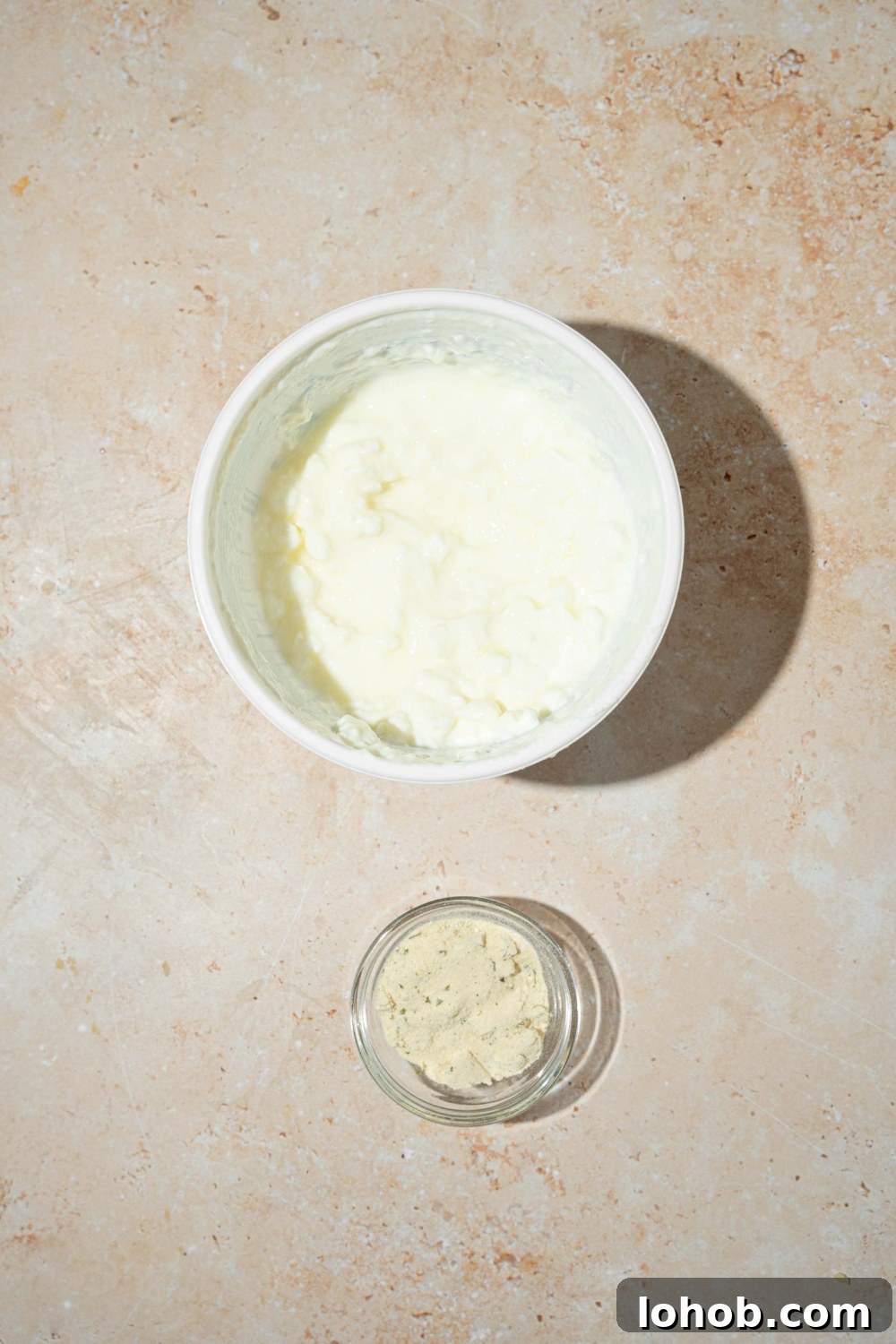 A tan counter with a bowl of cottage cheese and a bowl of ranch seasoning.