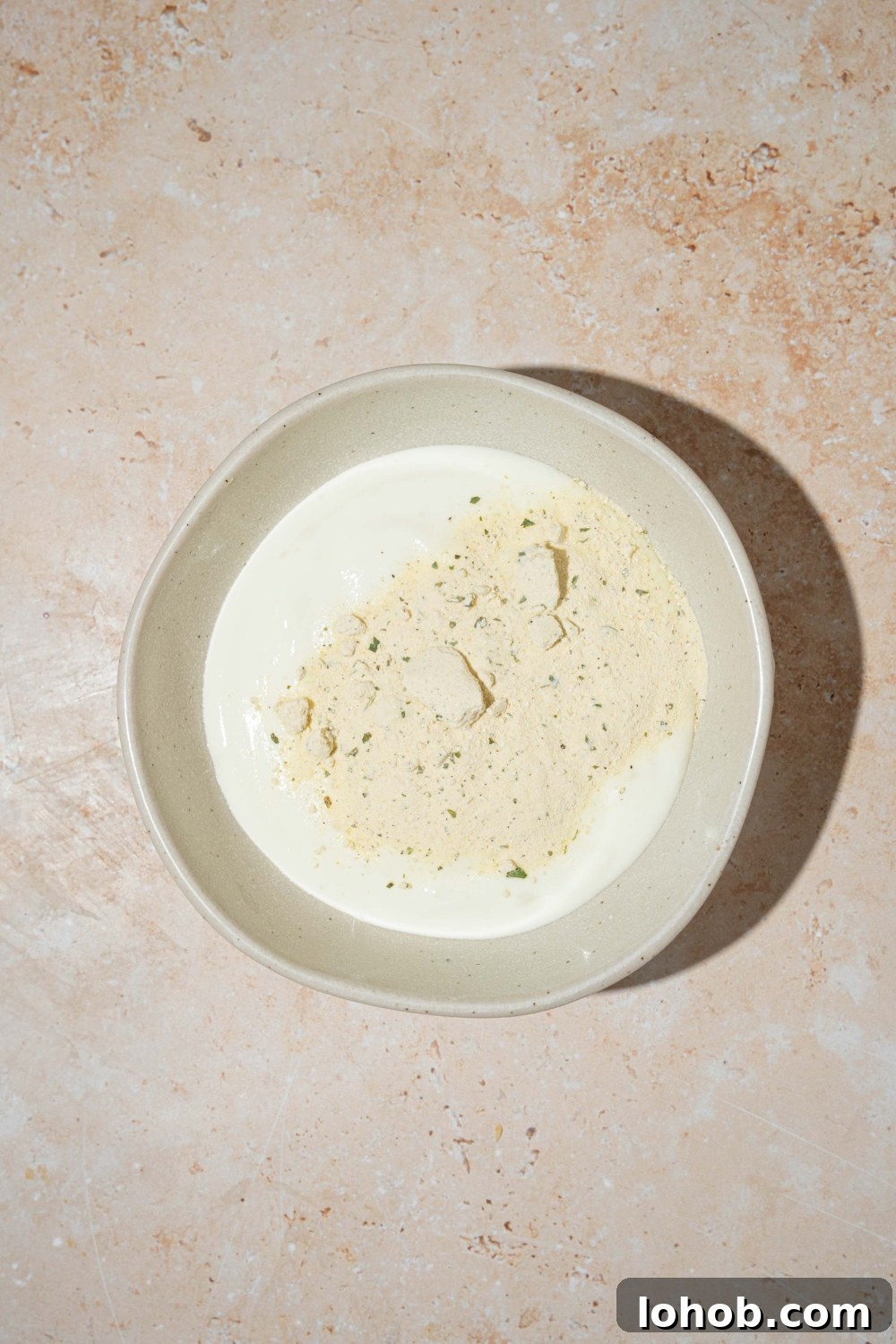 A white bowl with blended cottage cheese and ranch seasoning. The bowl is on a tan counter.