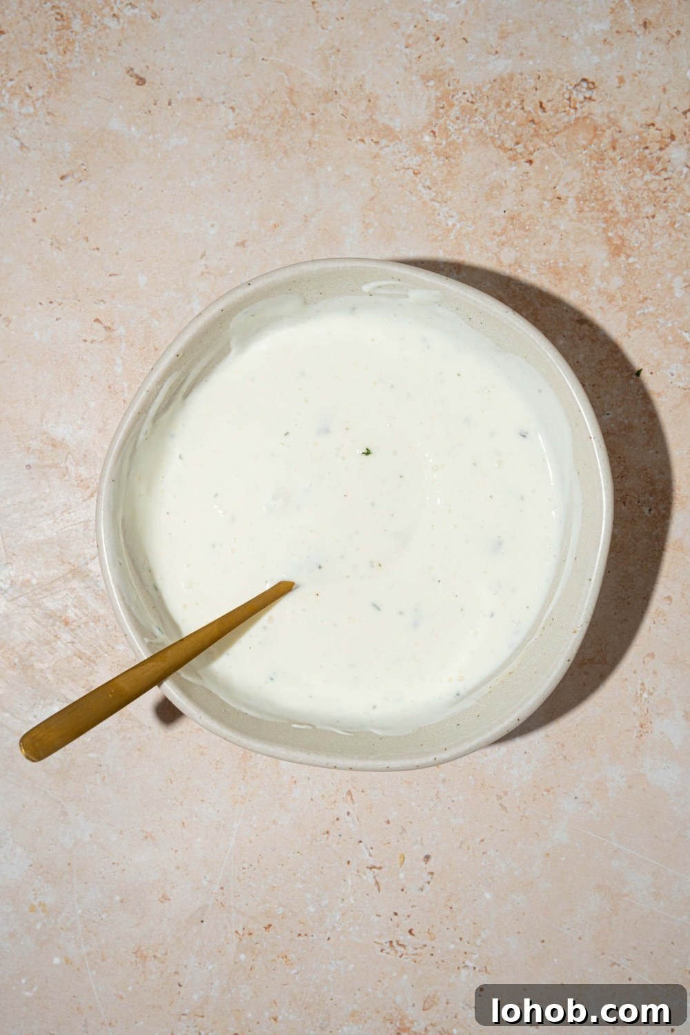 A white bowl with a spoon mixing cottage cheese ranch dip. The bowl is on a tan counter.