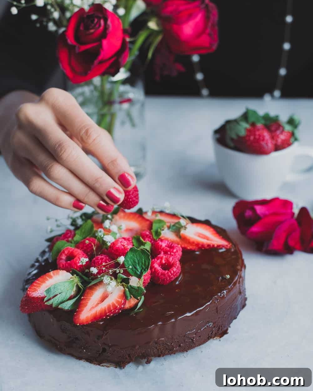 Woman placing berries all over chocolate cake on a white table.