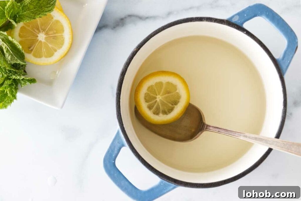 Classic Old-Fashioned Lemonade Recipe for Refreshing Summer Sips 5 a saucepan with simple syrup, slices of lemon and fresh mint in the upper left corner.