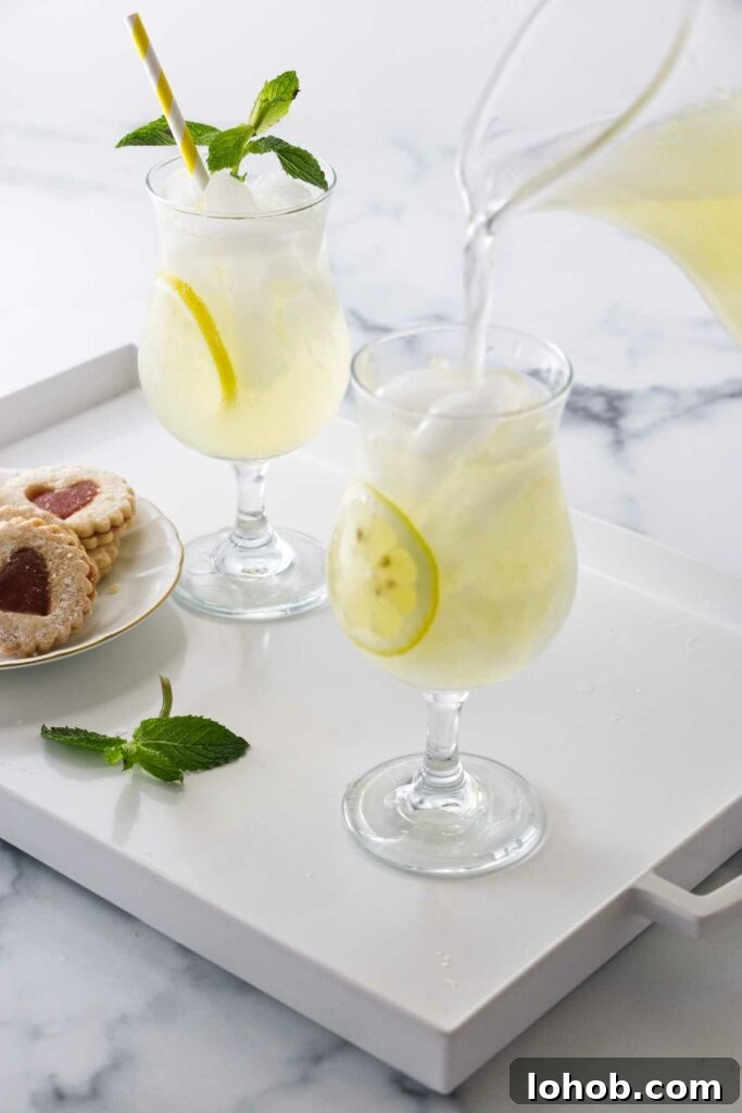 Classic Old-Fashioned Lemonade Recipe for Refreshing Summer Sips 6 A serving tray with two glasses of old fashioned lemonade, and a plate of cookies. A pitcher of lemonade filling a glass with ice.