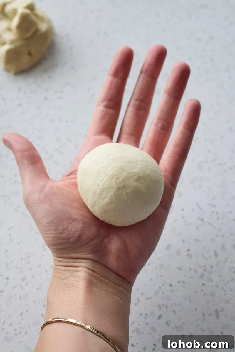 Fluffy Sourdough Discard Hamburger Buns You Can Make at Home 7 Dough rolled into a ball in the palm of a hand.
