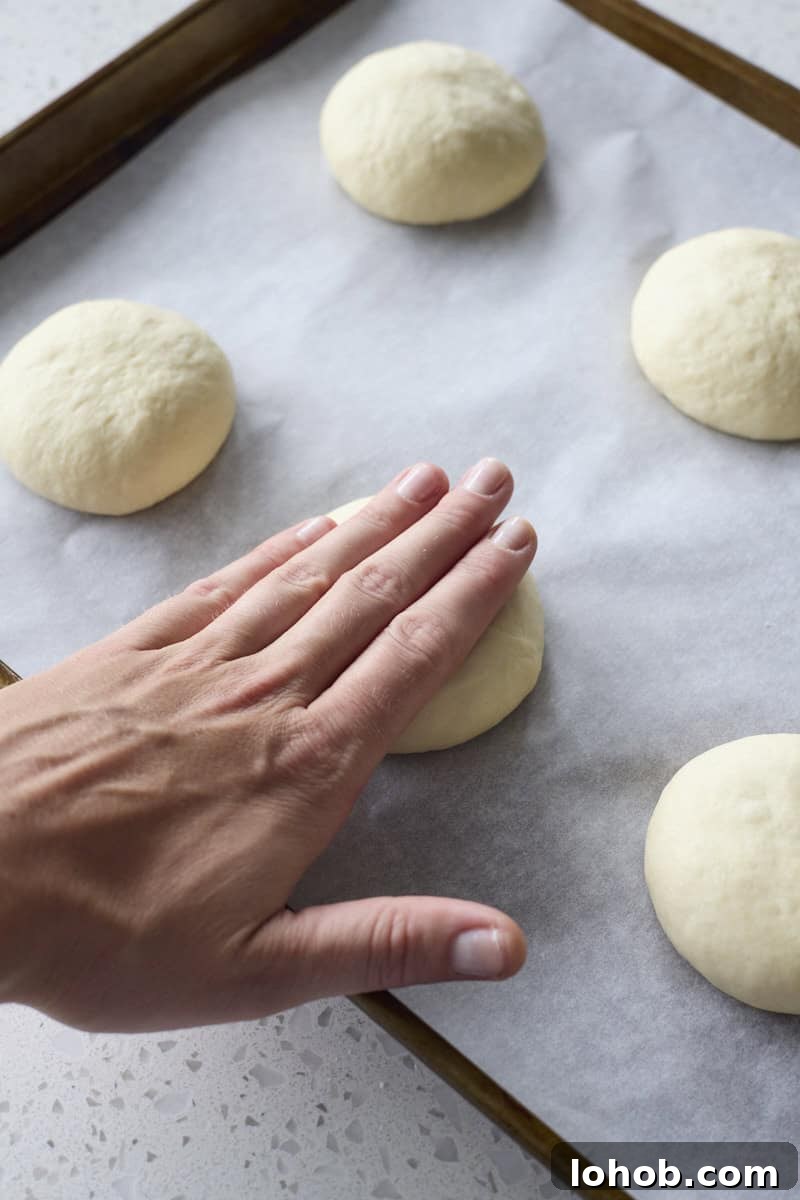Fluffy Sourdough Discard Hamburger Buns You Can Make at Home 8 A hand pressing the buns into disks.