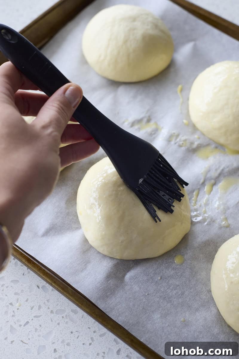 Fluffy Sourdough Discard Hamburger Buns You Can Make at Home 9 A hand brushing the buns with egg wash.