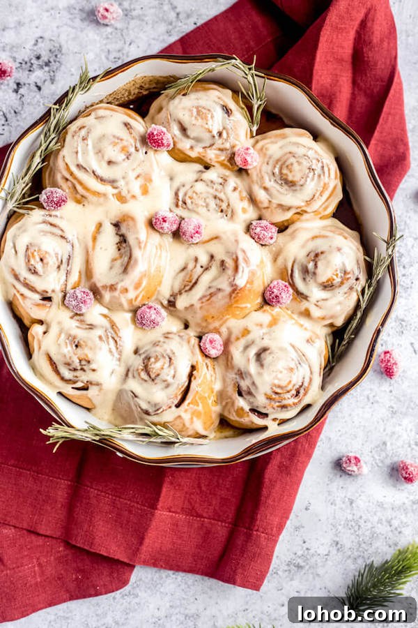 cinnamon rolls in a pie dish topped with sugared cranberries and rosemary 