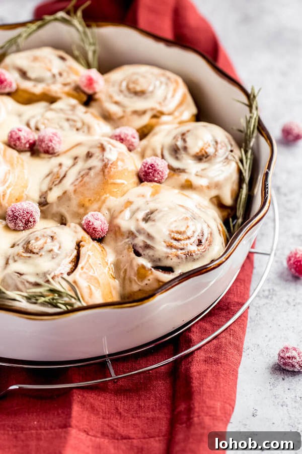 cinnamon rolls in a pie dish topped with sugared cranberries and rosemary 