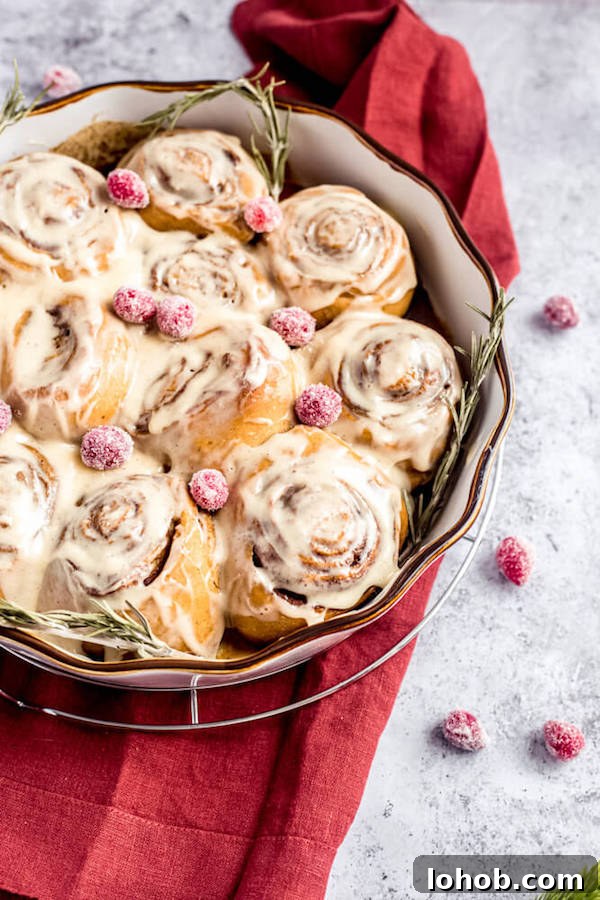 cinnamon rolls in a pie dish topped with sugared cranberries and rosemary 