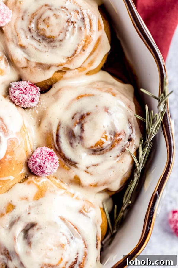 close up of cinnamon rolls topped with eggnog cream cheese icing and sugared cranberries