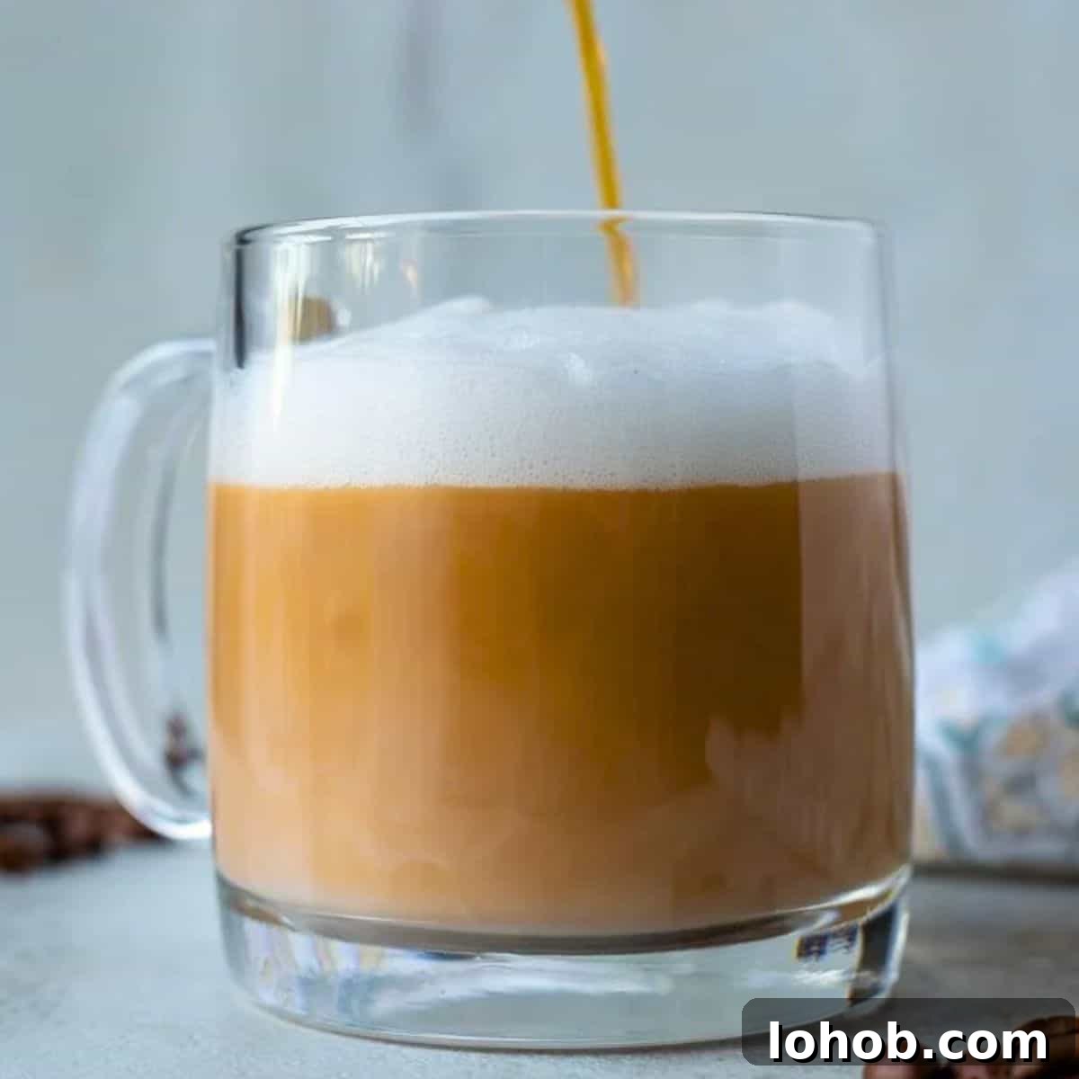 Coffee being poured into glass mug, creating distinct separate layers to form a homemade latte.