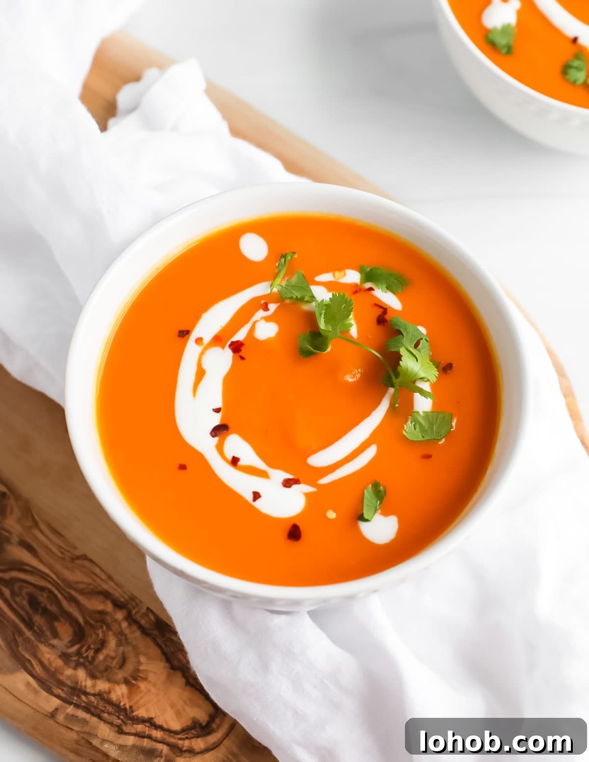 Creamy Carrot, Ginger and Coconut Soup 2 A white bowl filled with carrot soup that is topped with creamy coconut milk, fresh cilantro, and red pepper flakes.