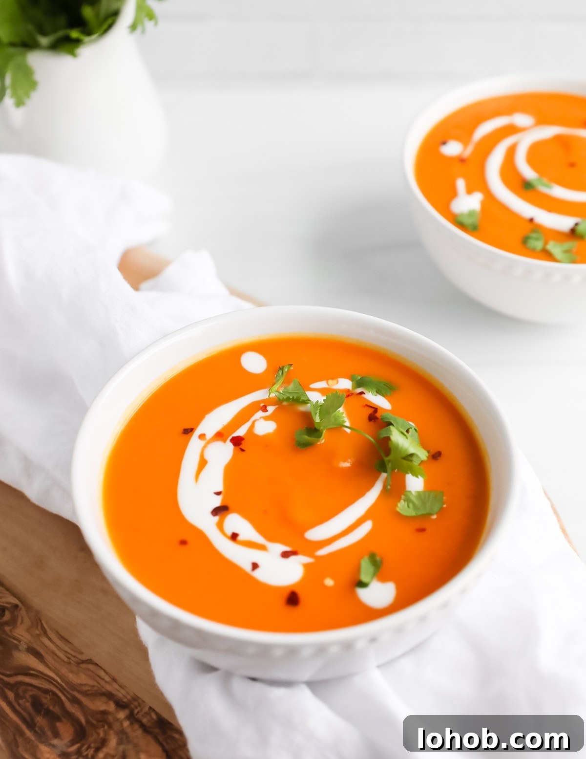 Creamy Carrot, Ginger and Coconut Soup 6 A large bowl filled with orange carrot soup that is garnished with coconut milk, cilantro, and crushed red pepper flakes.