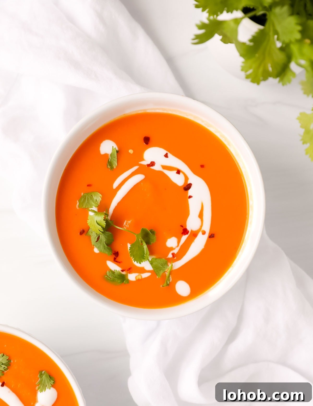 Creamy Carrot, Ginger and Coconut Soup 7 An overhead image of a bowl of carrot soup that is topped with coconut milk, cilantro, and red pepper flakes.