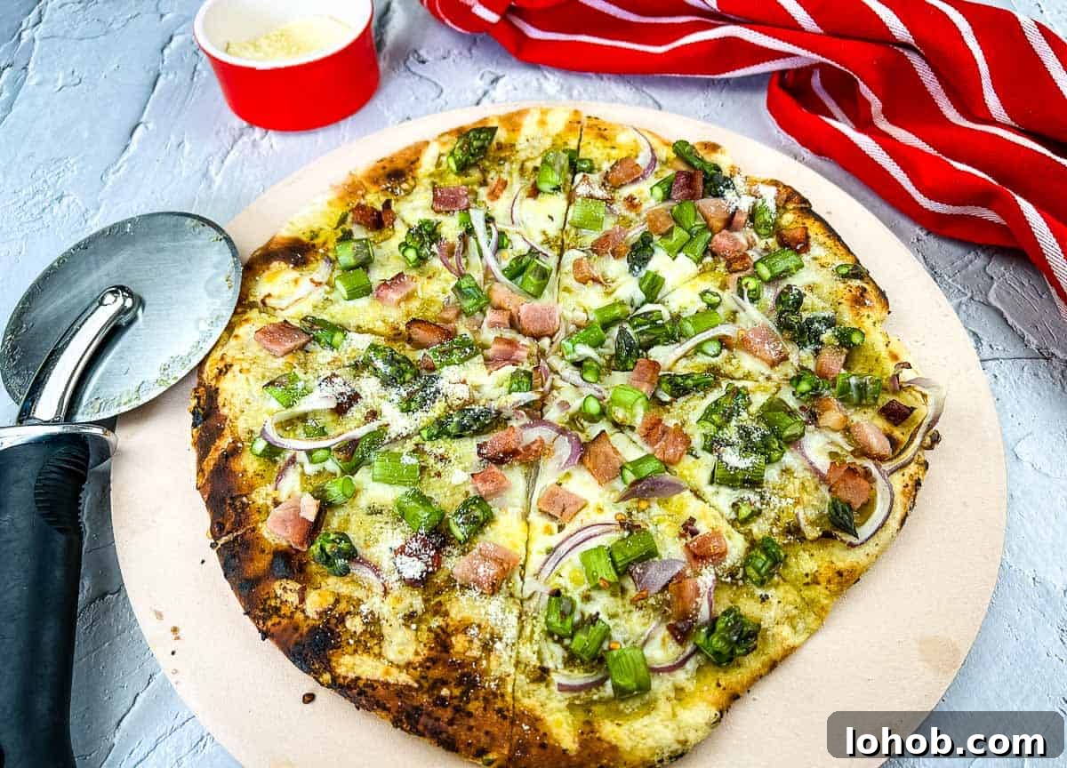 A pizza with ham and asparagus on a pizza stone.