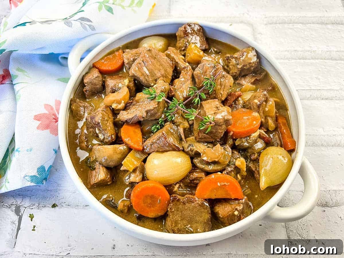 Beef bourguignon in a white bowl with thyme.