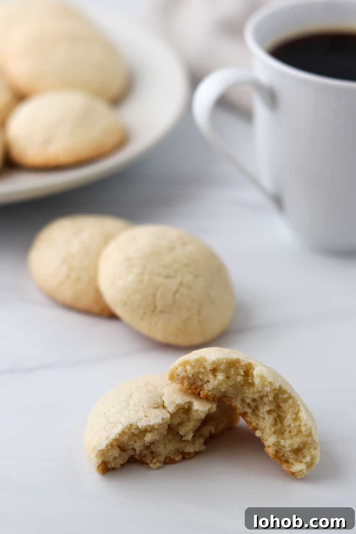 Almond Macaroon broke in half next to a cup of coffee.