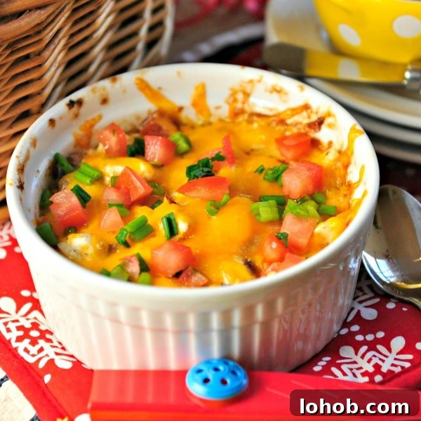 white bowl of cheesy dish covered with tomatoes and scallions