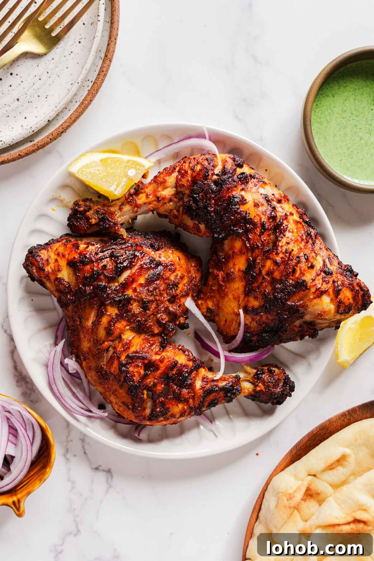 Crispy Air Fryer Tandoori Chicken Recipe 2 air fryer tandoori chicken on a plate with onion and green chutney on the side.