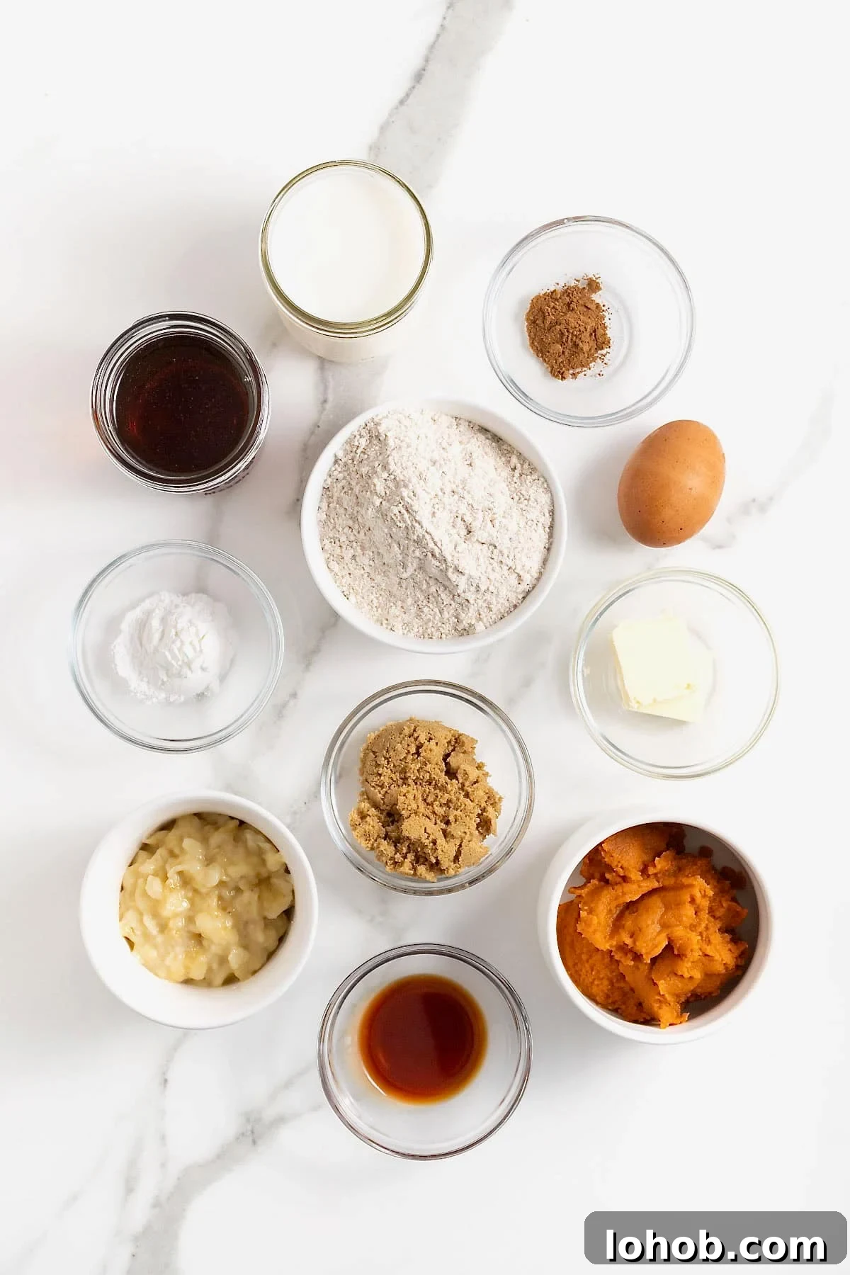Ingredients to make pumpkin banana pancakes in small glass dishes on a white marble counter.
