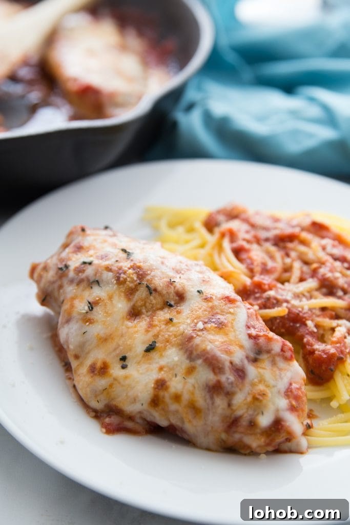 Top Weight Watchers Chicken Recipes: Quick Low-Point Meals 5 Chicken breast topped with tomato sauce and melted cheese next to spaghetti and tomato sauce on a white plate- the rest of the pan of chicken sits in the background
