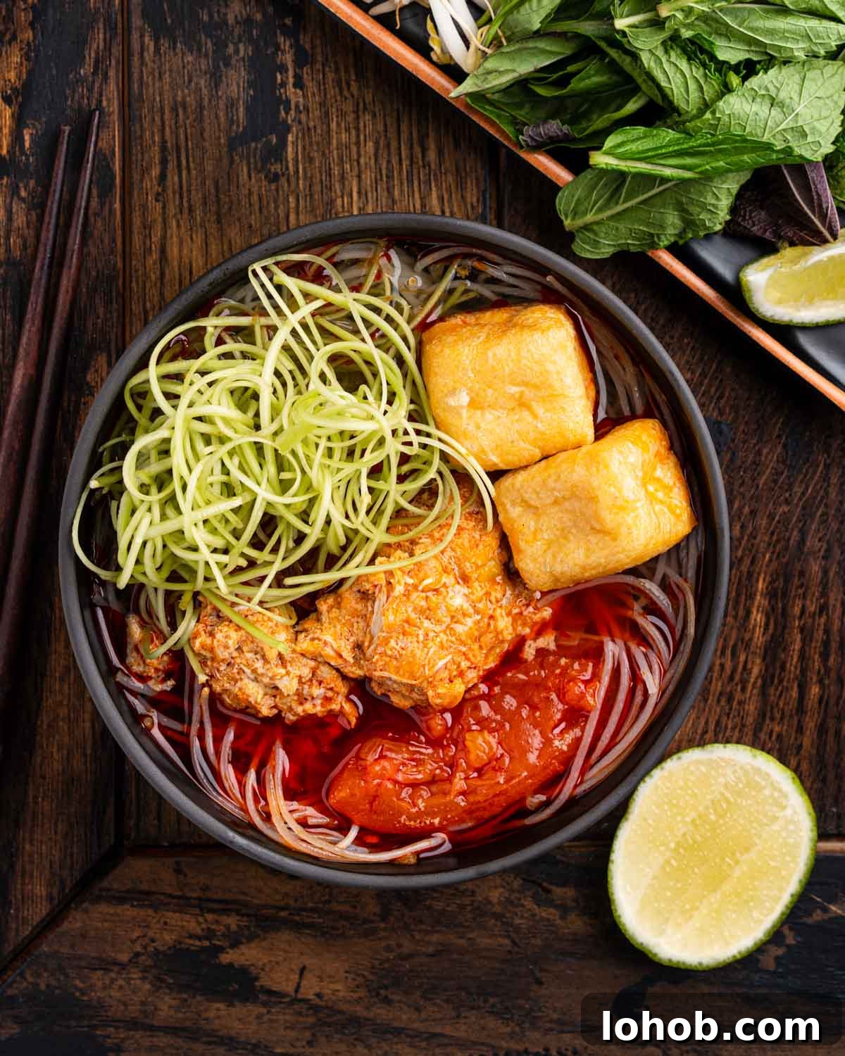 bowl of bun rieu topped with fried tofu, shredded rau muong and lime wedge.