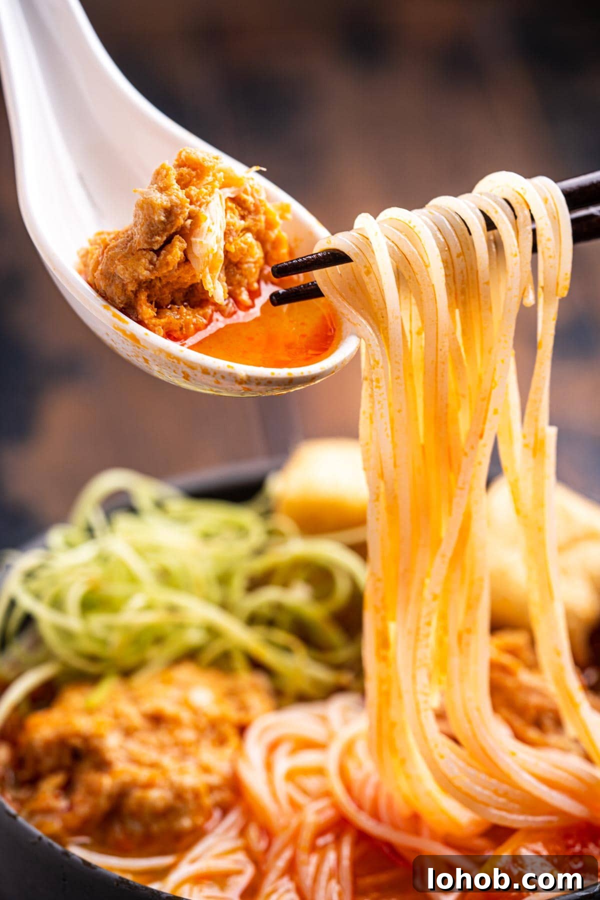 Spoon holding up broth and a piece of crab meatball; chopsticks holding up noodles.