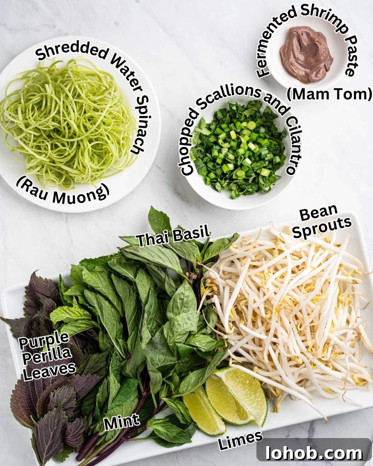 Toppings for bun rieu on plates and bowls: shredded water spinach, fermented shrimp paste (mam tom), chopped scallions and cilantro, purple perilla leaves, mint, Thai basil, bean sprouts, and lime wedges.