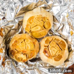 Close up photo of three bulbs of roasted garlic in foil