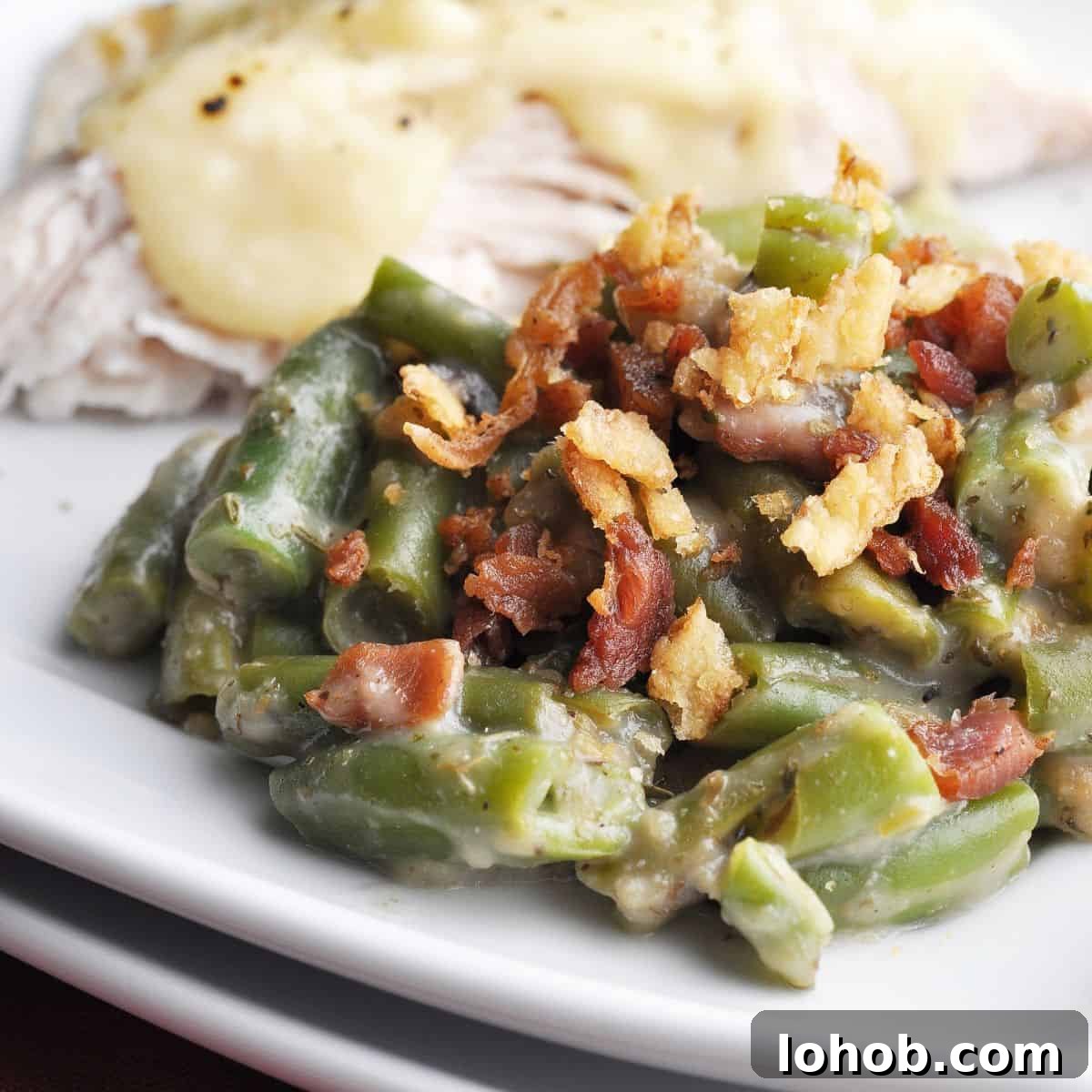 Green bean casserole topped with fried onions and bacon on plate with turkey covered in gravy.