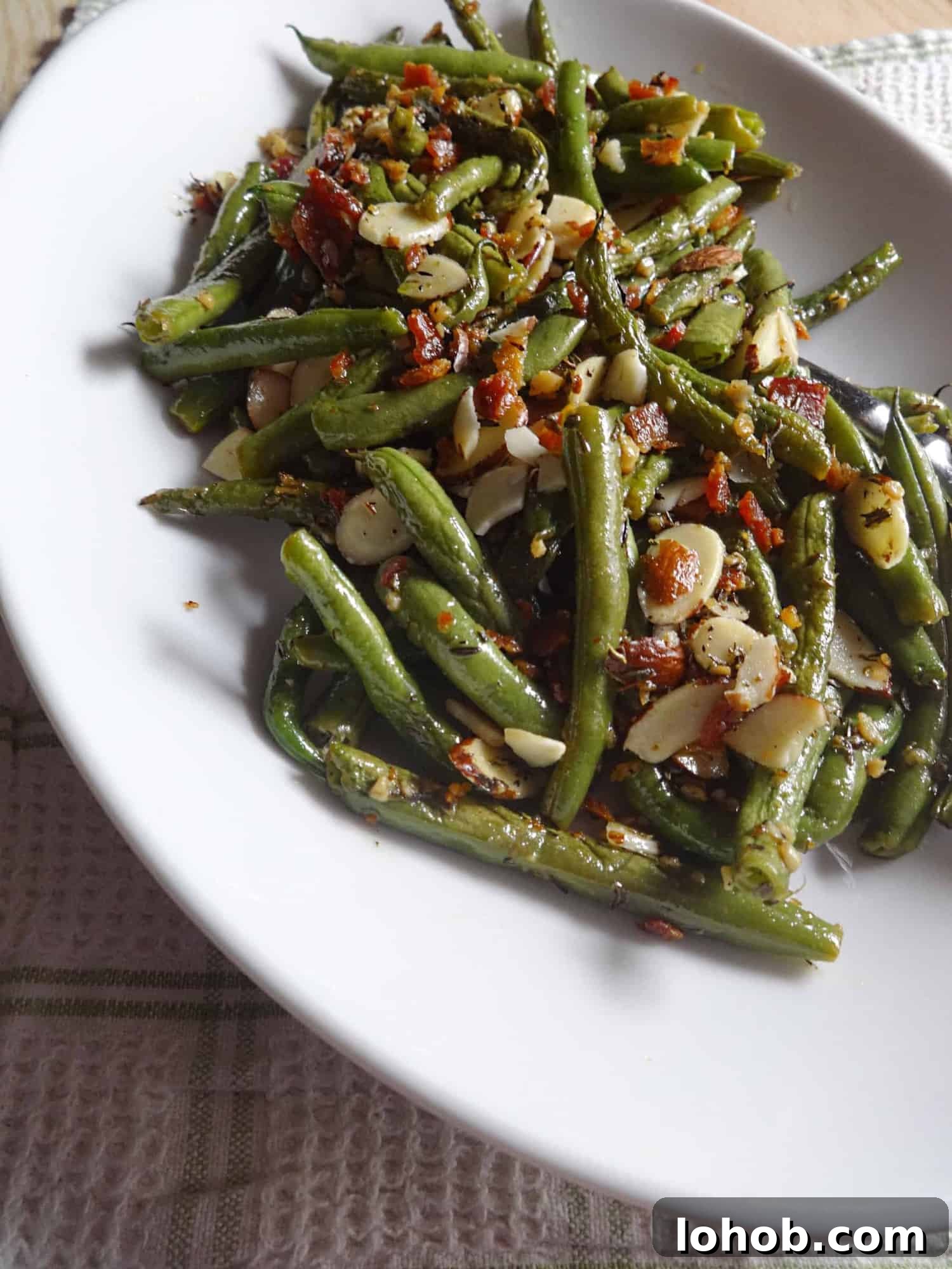 Cooked green beans, slivered almonds, and bacon served on plate.