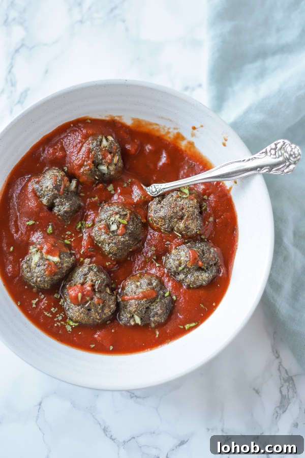 paleo meatballs in marinara sauce in a white bowl on a marble countertop with a teal napkin to the right