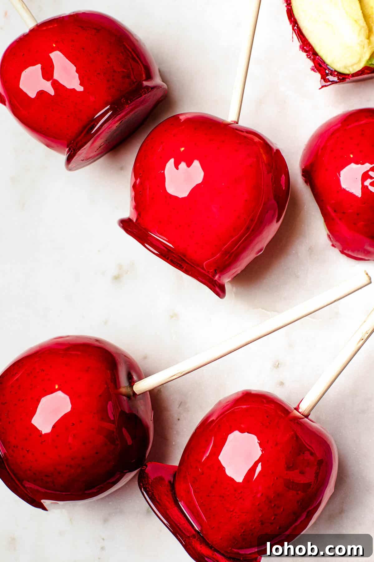 Several candy apples on a white cutting board. Plain Granny Smith apples and an orange fringed placemat in the background.