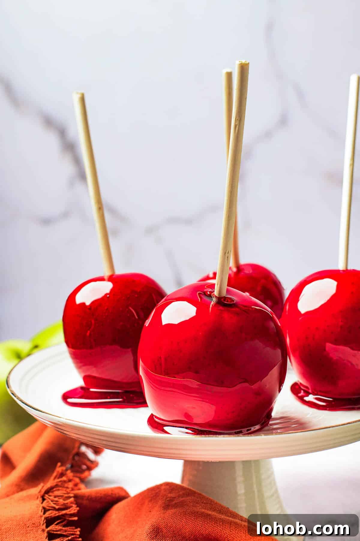 A white cake stand with four candied apples displayed on it.