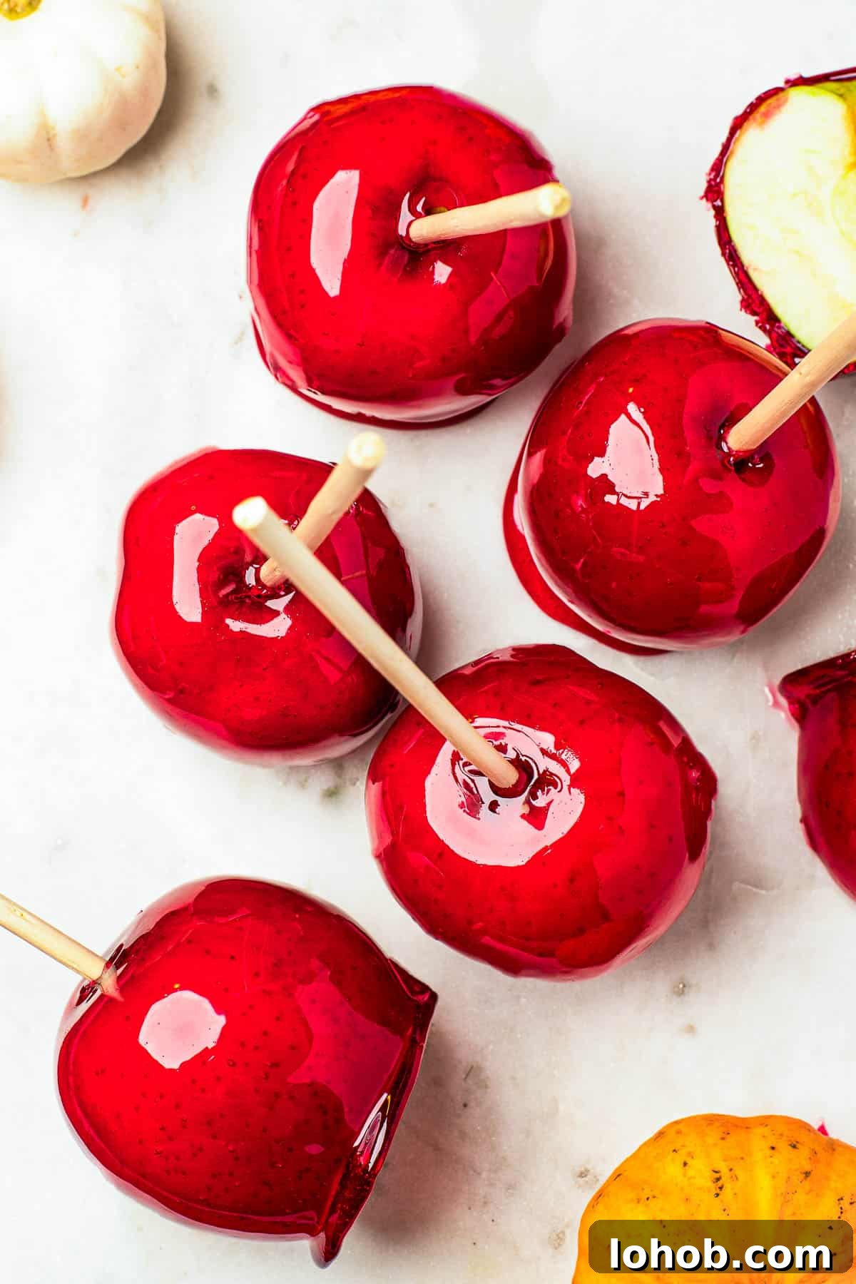 Several candy apples on a white cutting board. Plain Granny Smith apples and an orange fringed placemat in the background.