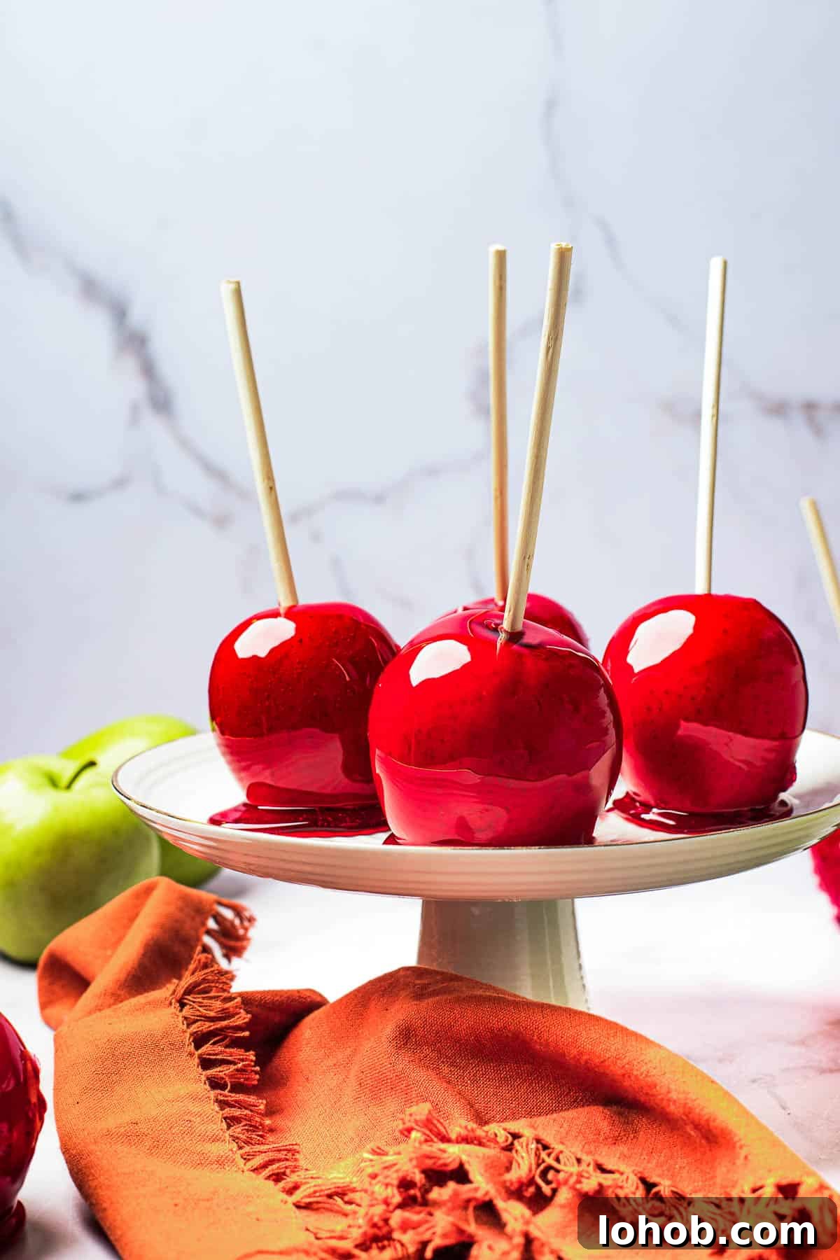 A white cake stand with four candied apples displayed on it.