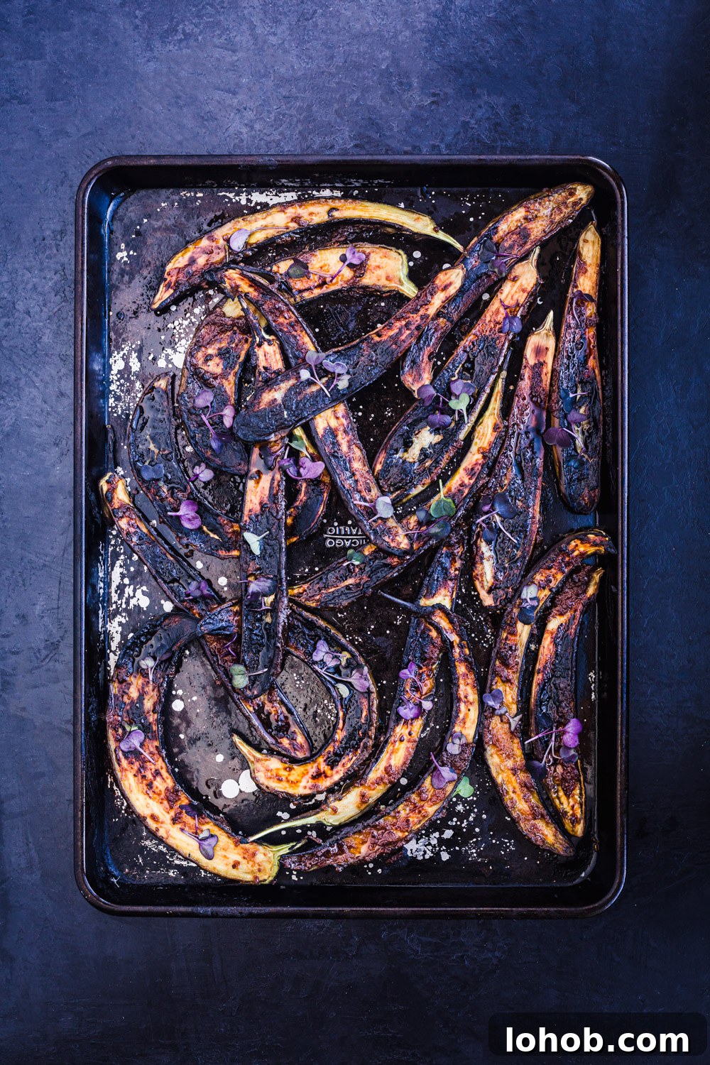 Ginger-miso glazed eggplant on a baking sheet, just out of the oven and topped with micro greens and flaky sea salt.