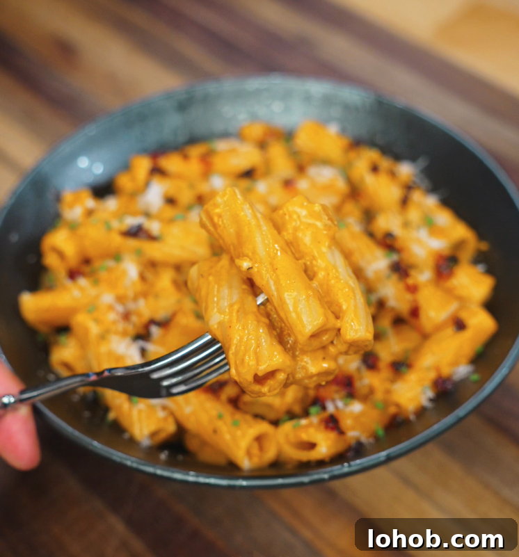 Creamy Gochujang Pasta Recipe 3 A fork lifting a bite of creamy gochujang rigatoni from a full bowl, showcasing the rich orange sauce clinging to each tube of pasta.