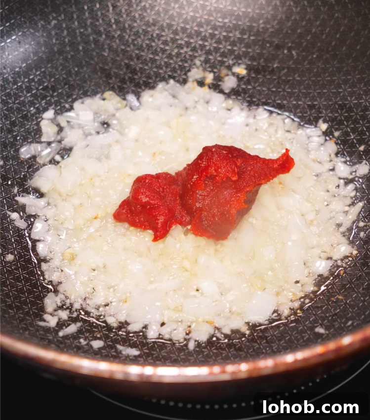 Creamy Gochujang Pasta Recipe 4 A close-up of sautéed diced onions with vibrant red gochujang and tomato paste sizzling in a nonstick skillet, creating a savory, spicy base for the sauce.